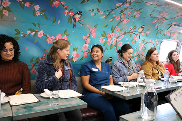 group of people smiling at table in front of a wall with floral design